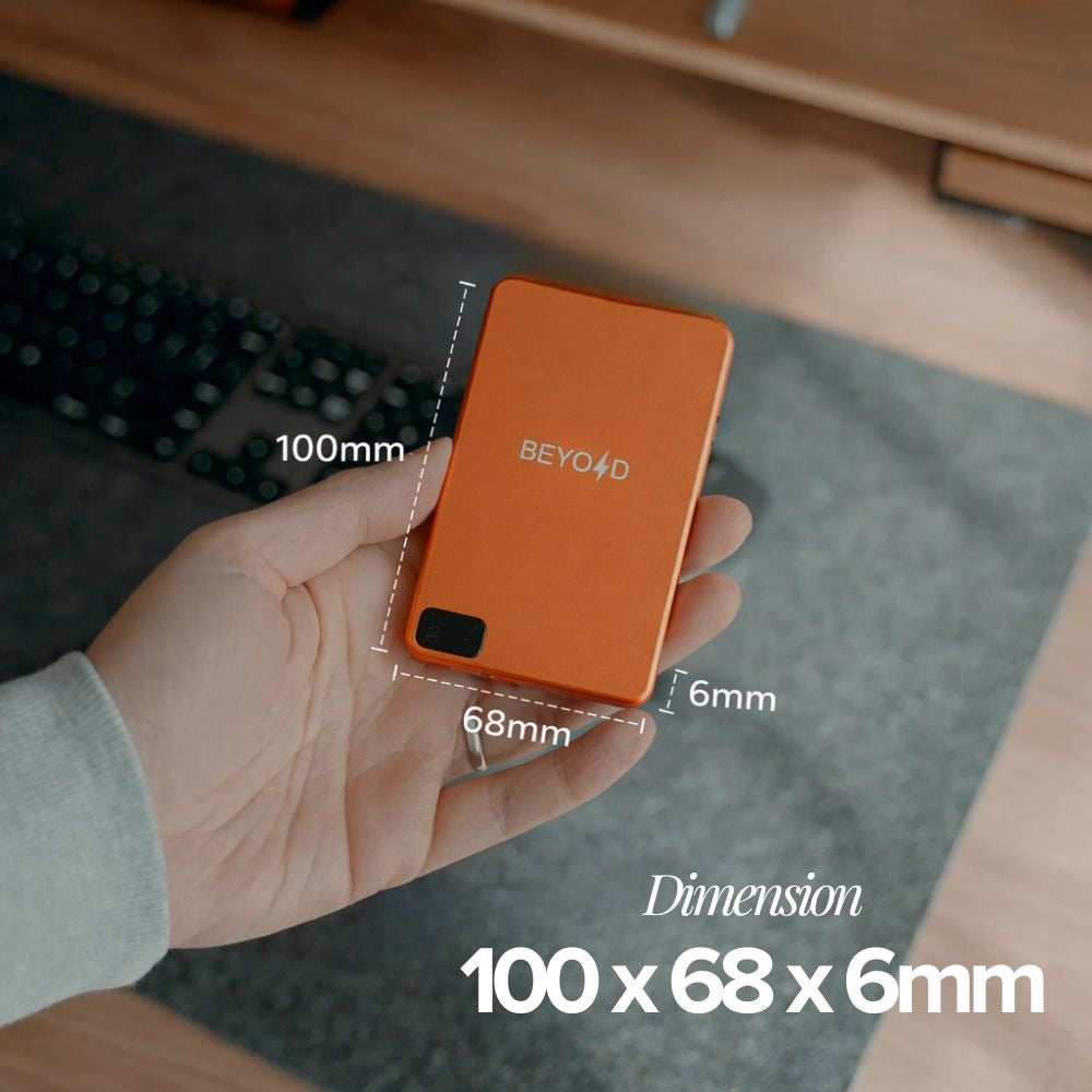 Hand holding an orange external hard drive with dimensions labeled, on a desk.